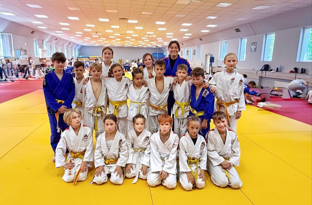 Dzieci i trenerka w kimonach pozują na żółtej macie podczas obozu judo w Cetniewie