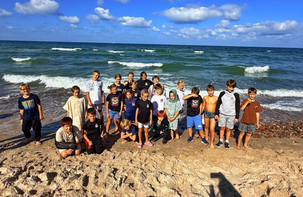 Duża grupa dzieci i opiekunów stoi na plaży nad morzem podczas obozu judo w Cetniewie