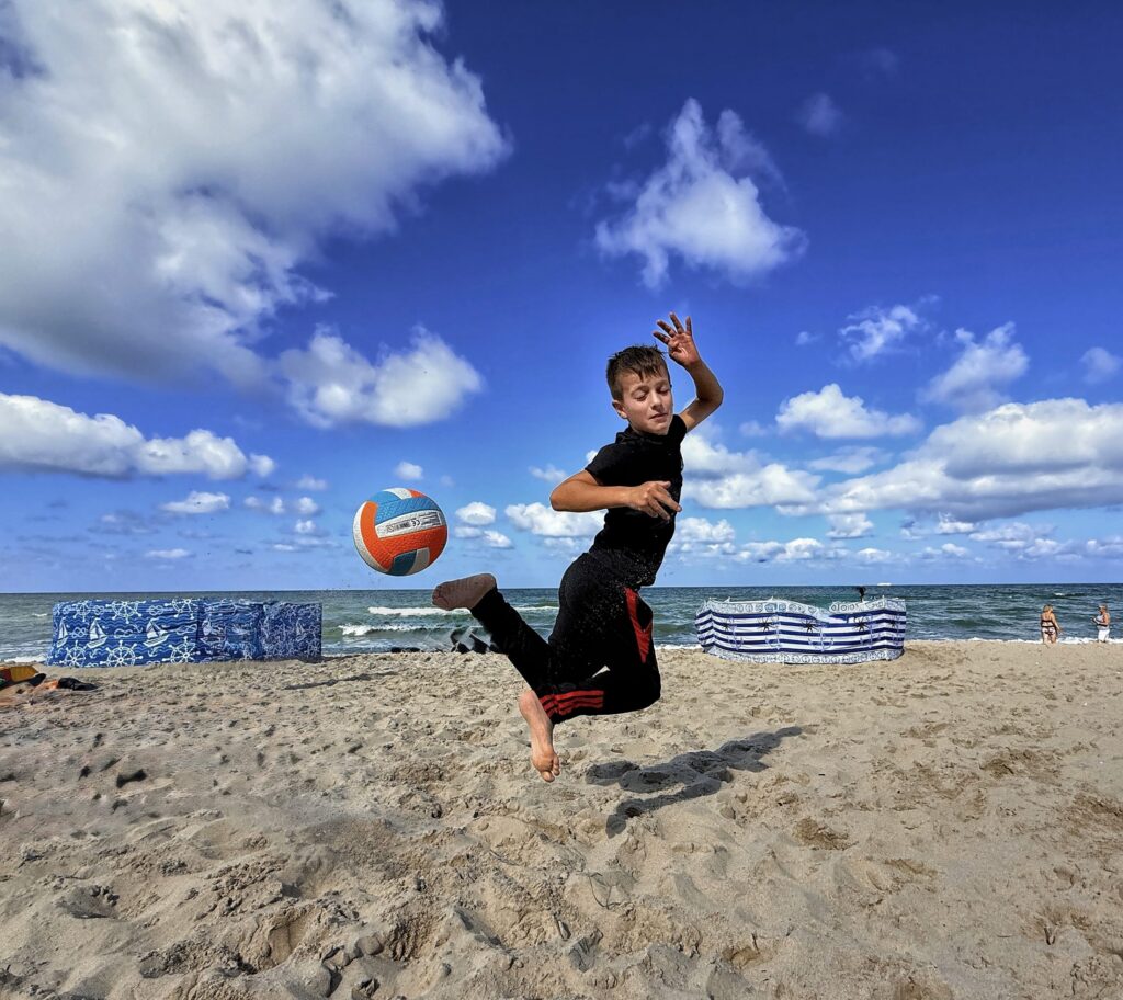 Chłopiec skacze do siatkówki na plaży pod błękitnym niebem podczas obozu judo w Cetniewie
