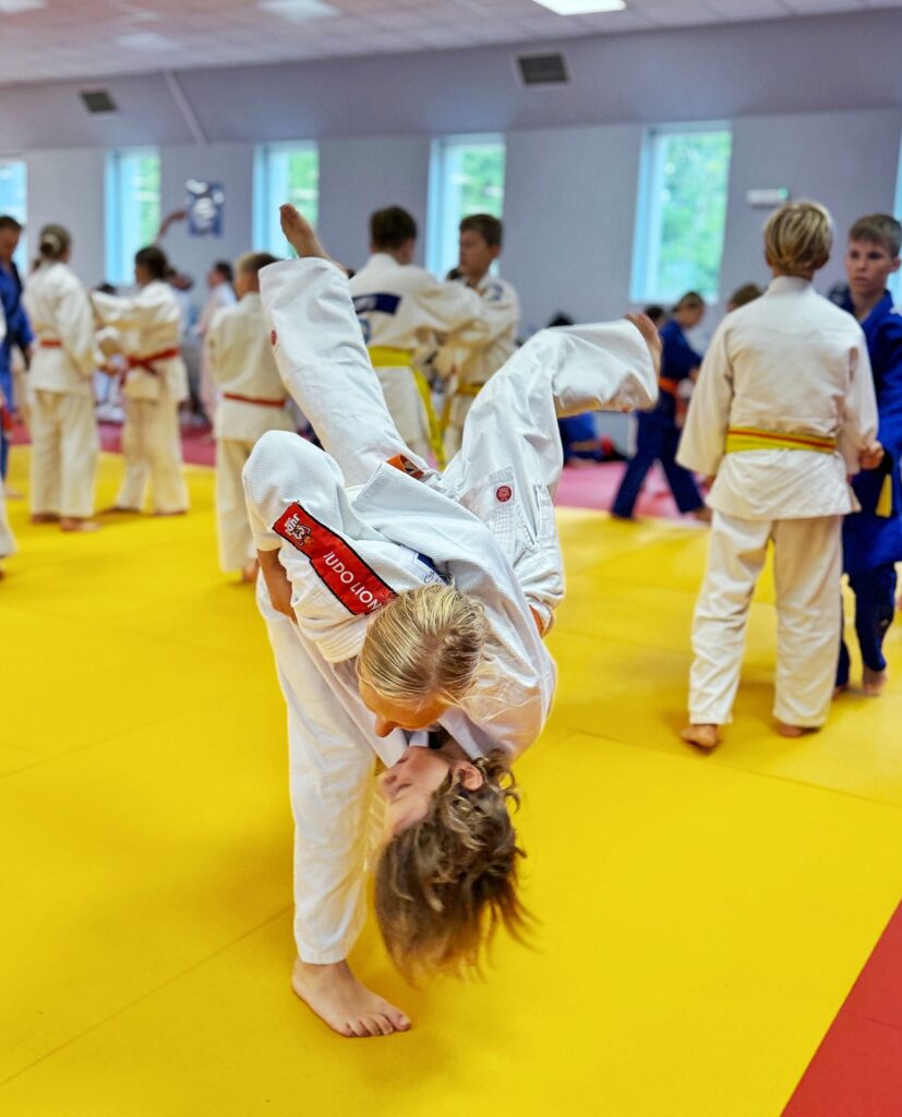 Zawodniczka w kimono Judo Lion wykonuje dynamiczny rzut partnerki na żółtej macie