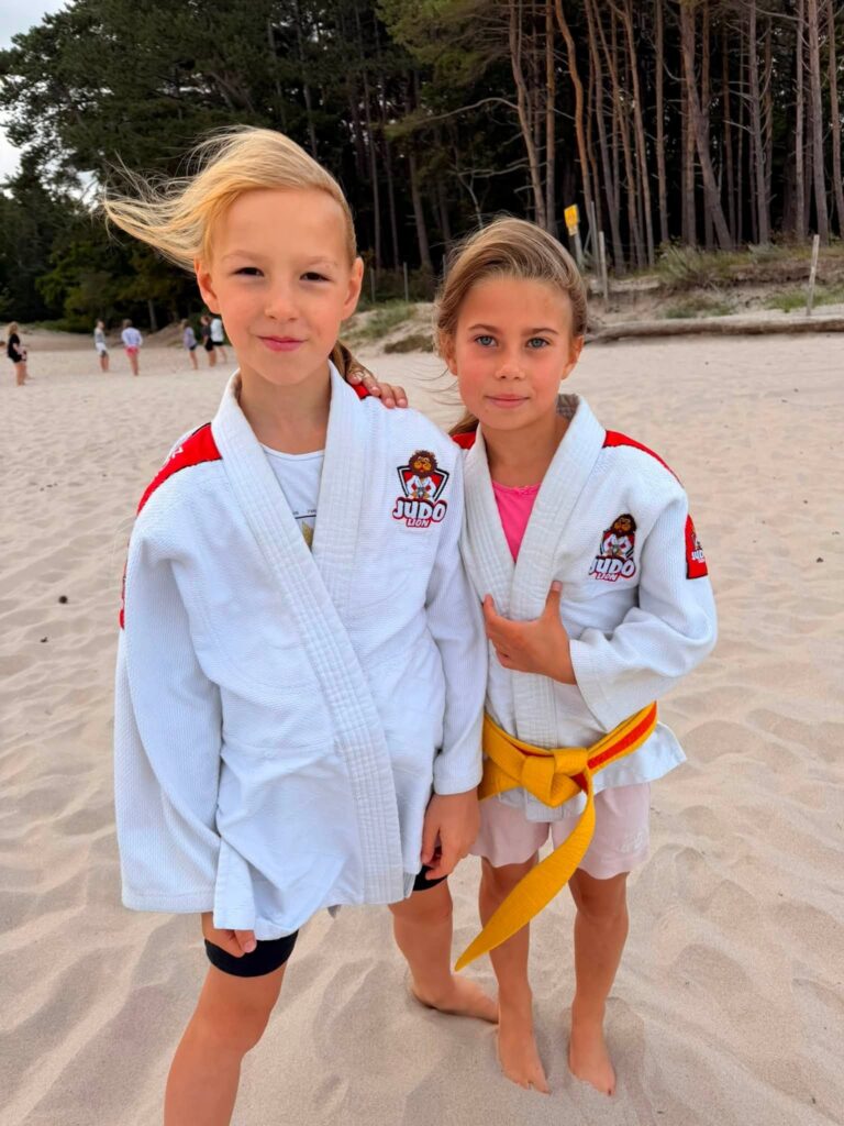Dwie zawodniczki w kimonach Judo Lion stoją na plaży w Jarosławcu