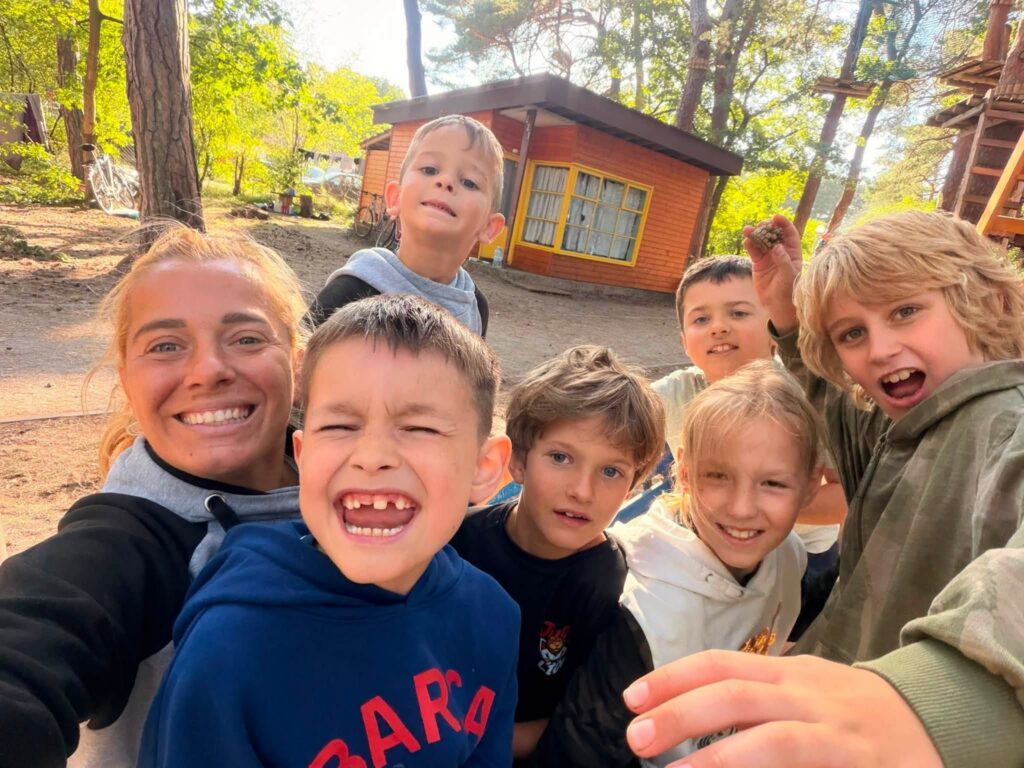 Uśmiechnięta grupa dzieci i opiekunki robi selfie wśród sosen na obozie w Jarosławcu